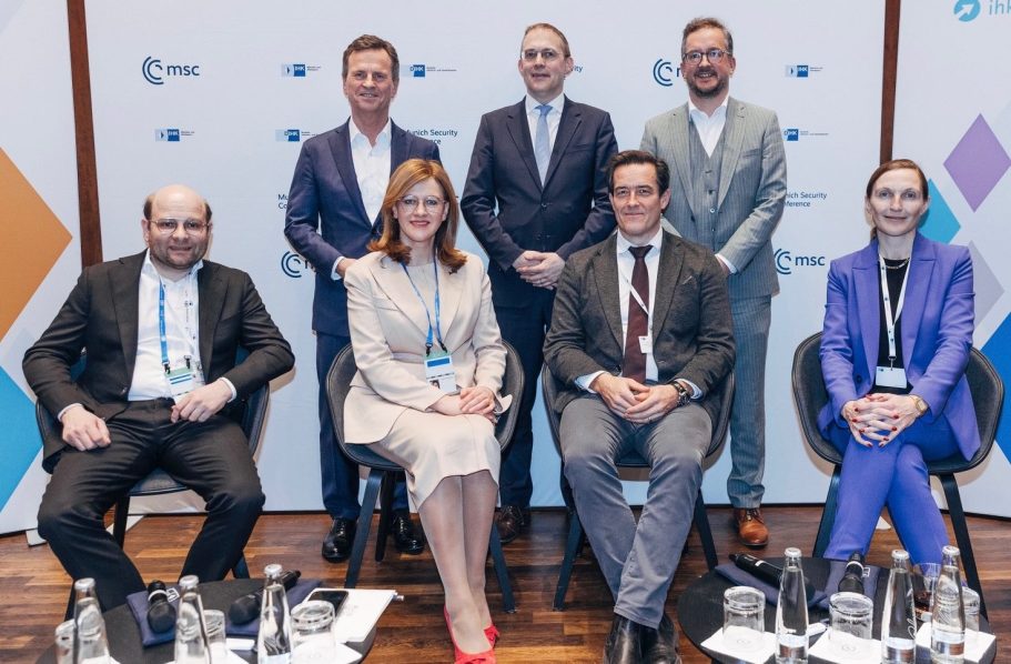 Panel an der IHK München Sieben Personen in formeller Kleidung sitzen und stehen vor einem Hintergrund mit Logos.
